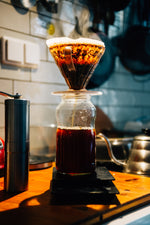A pourover coffee being brewed using a V60 above a carafe in a coffee shop sitting on the bar.